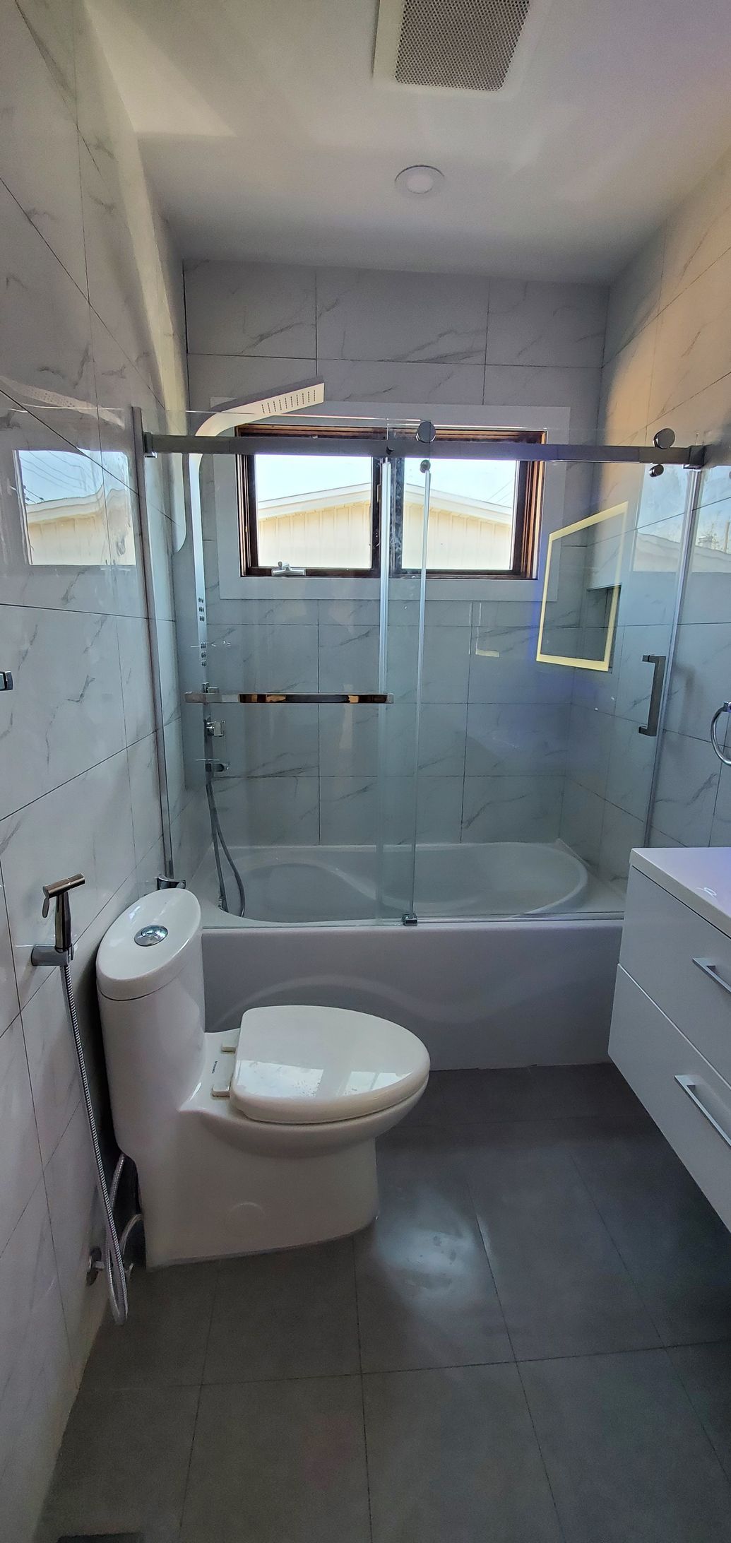A bathroom with a toilet , tub , shower and window.
