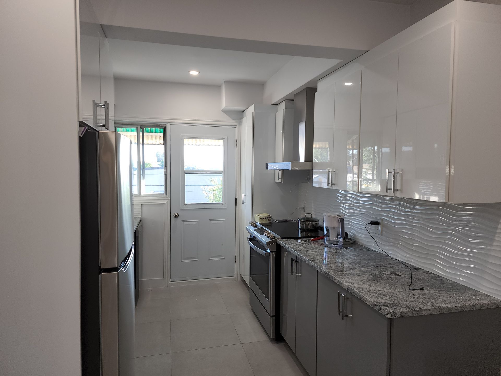 A kitchen with white cabinets , granite counter tops , stainless steel appliances and a refrigerator.