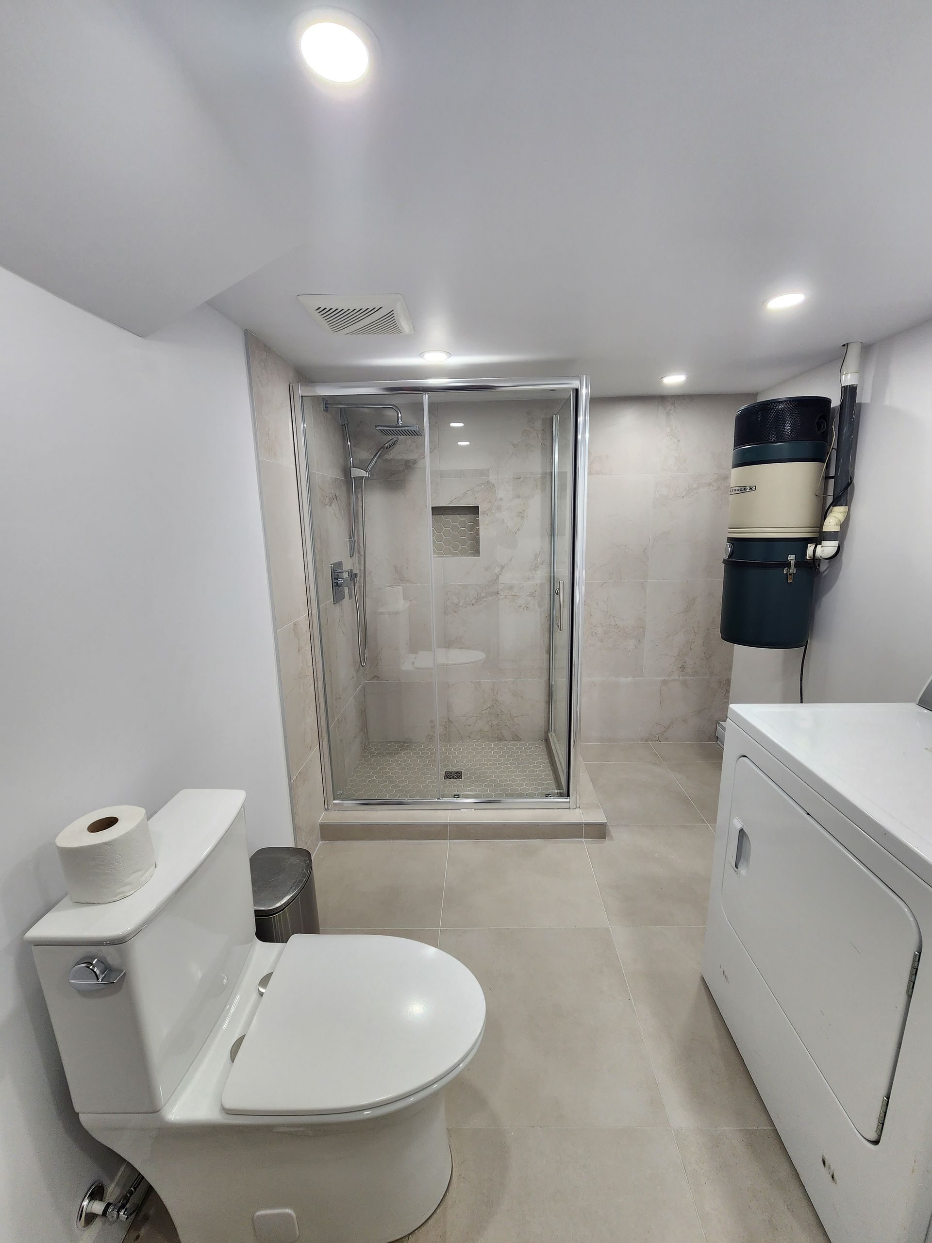A bathroom with a toilet , shower , washer and dryer.