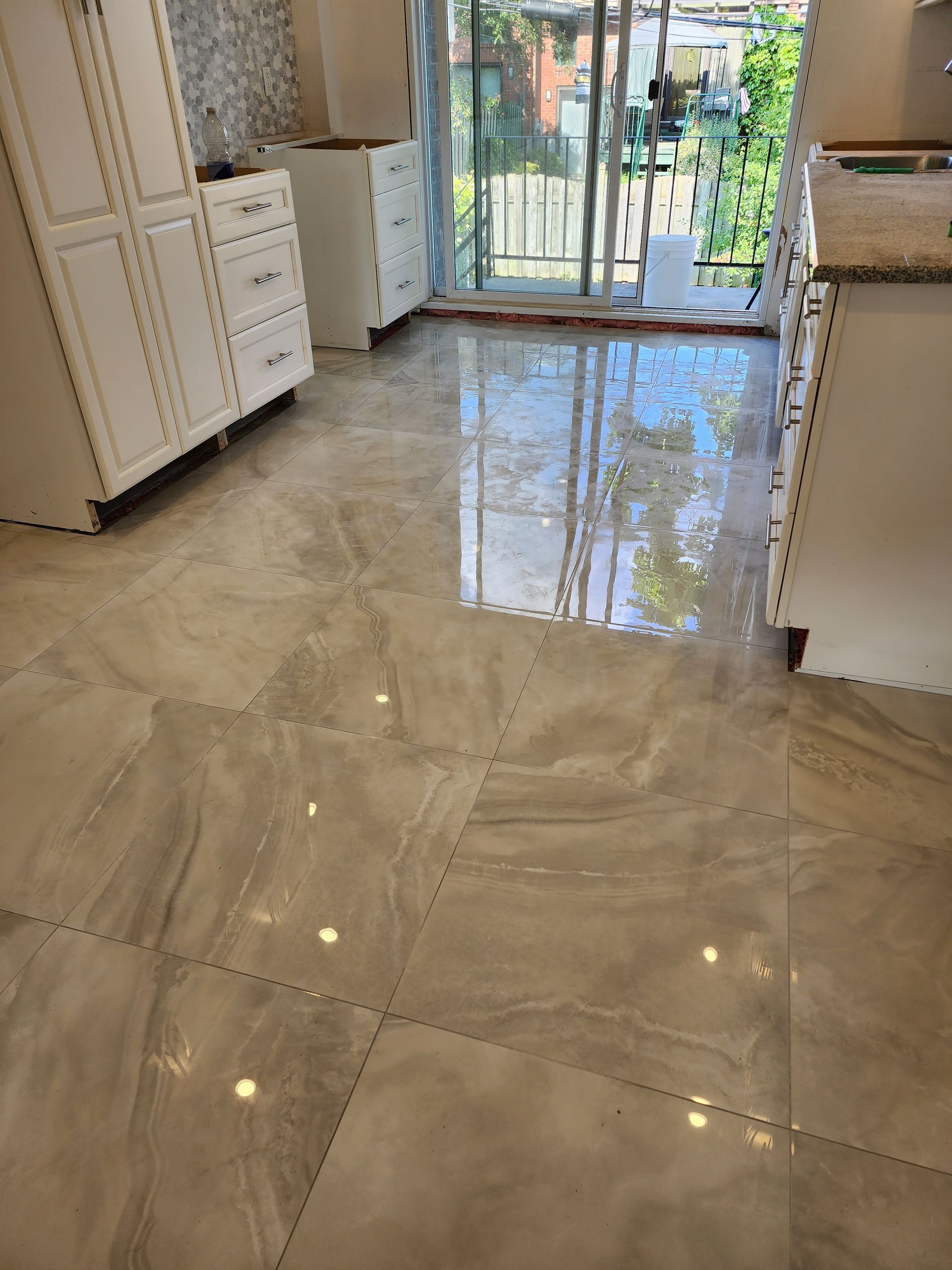 A kitchen with a tiled floor , white cabinets , and a sliding glass door.