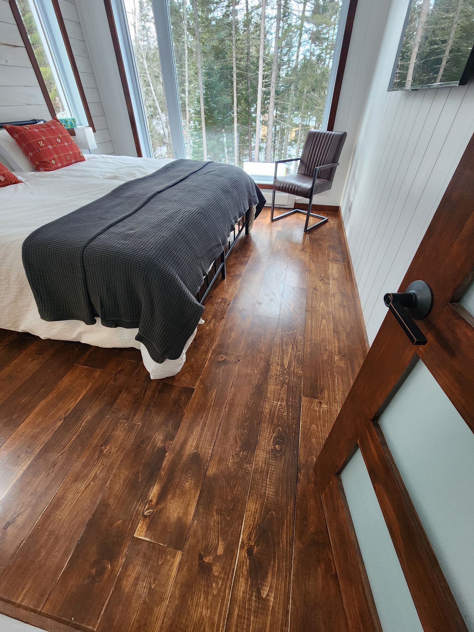 A bedroom with a bed , chair , and large windows.
