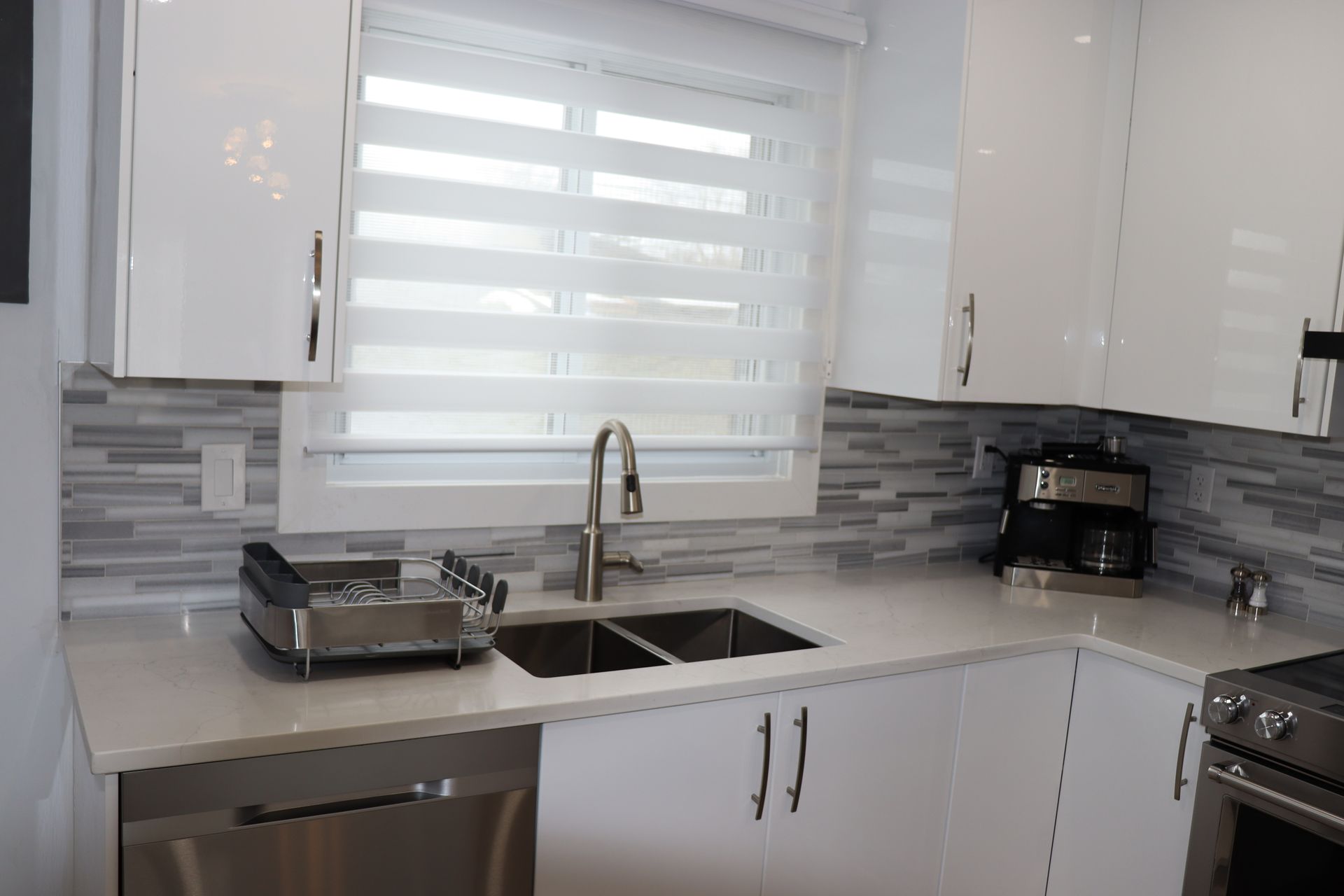 A kitchen with white cabinets , stainless steel appliances , a sink and a window.