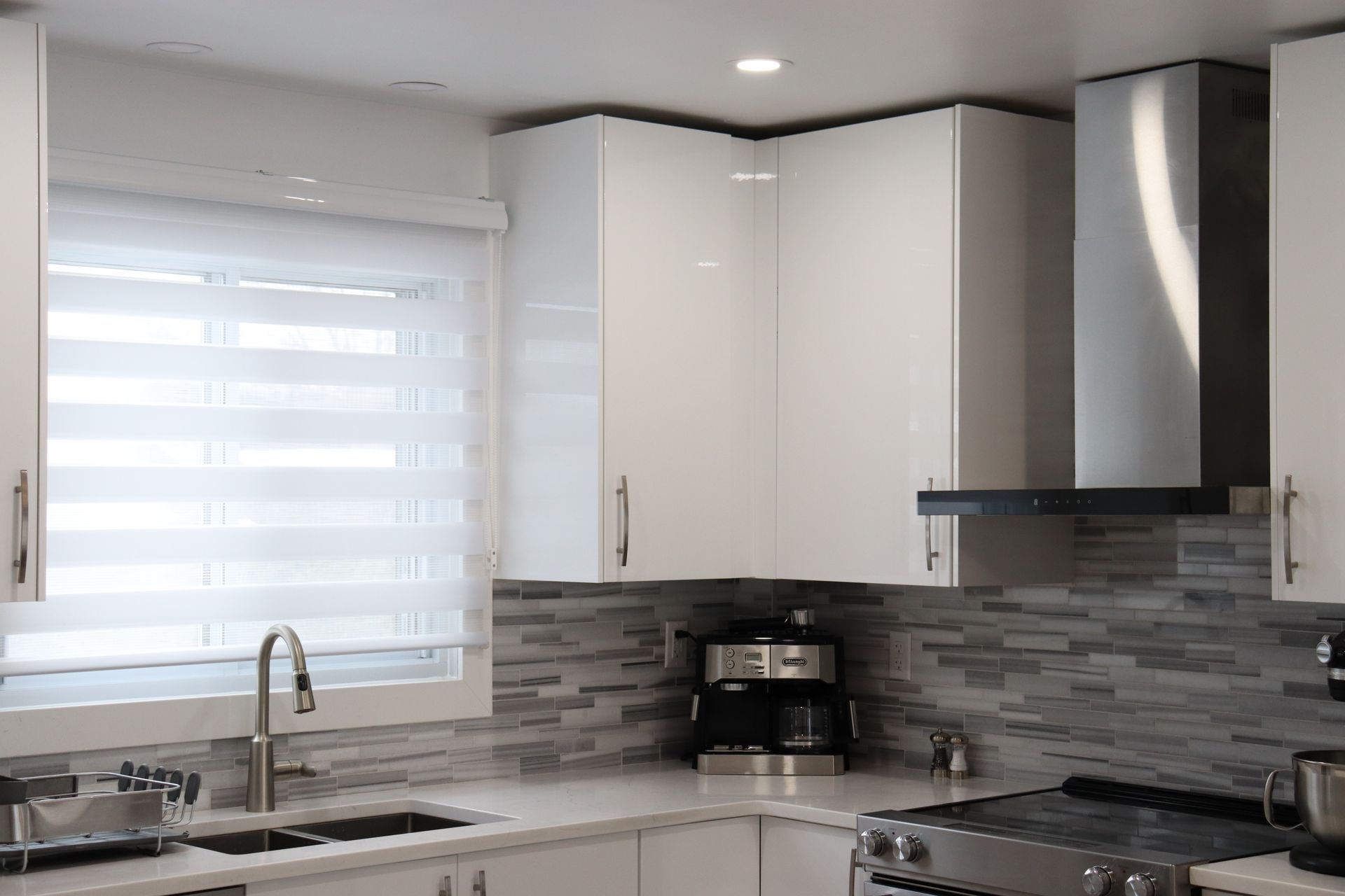 A kitchen with white cabinets , a stove , a sink , and a window.