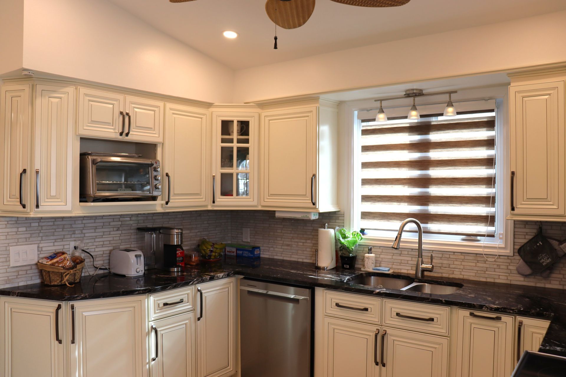 A kitchen with white cabinets , black counter tops , stainless steel appliances and a ceiling fan.