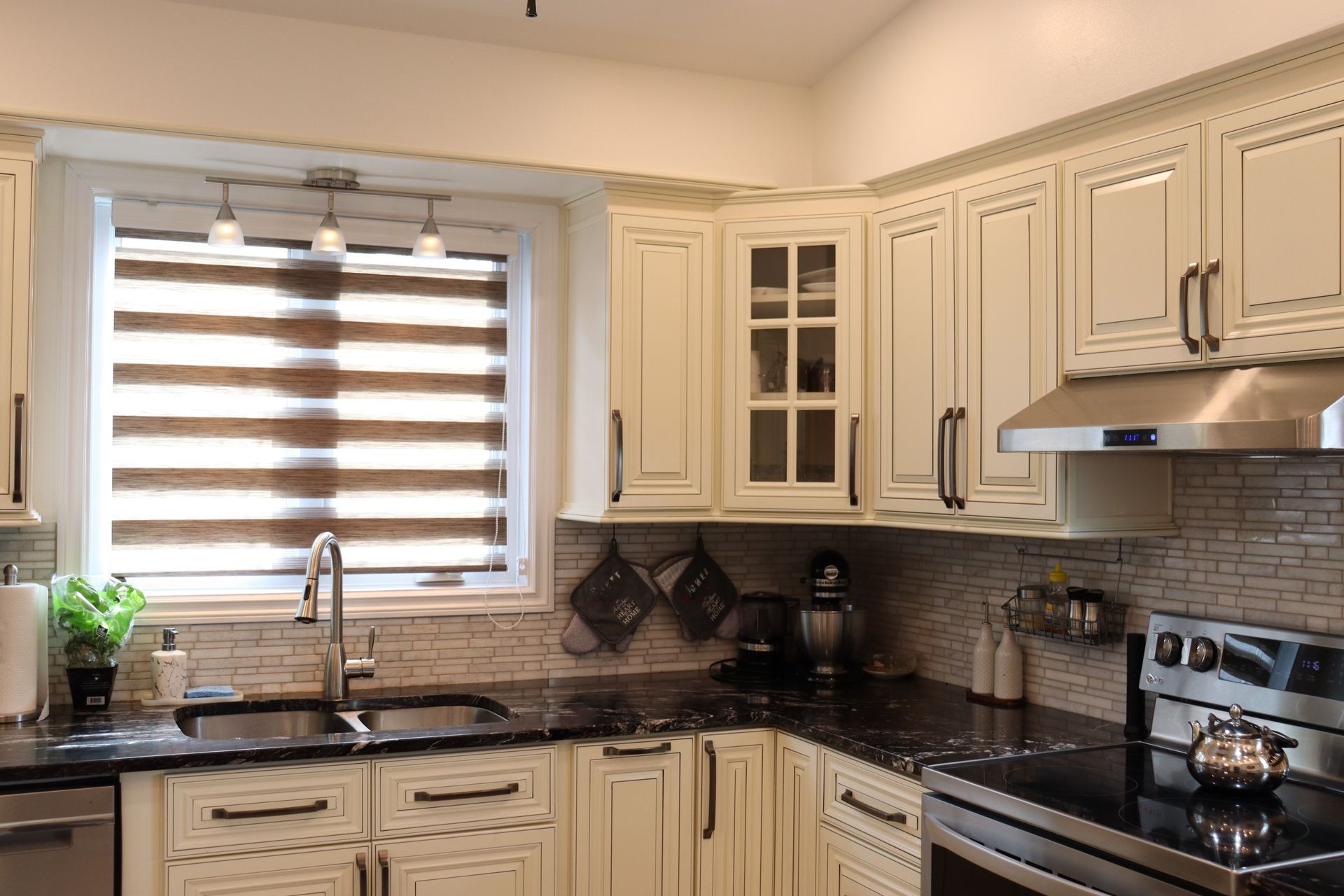 A kitchen with white cabinets , black counter tops , stainless steel appliances and a window.