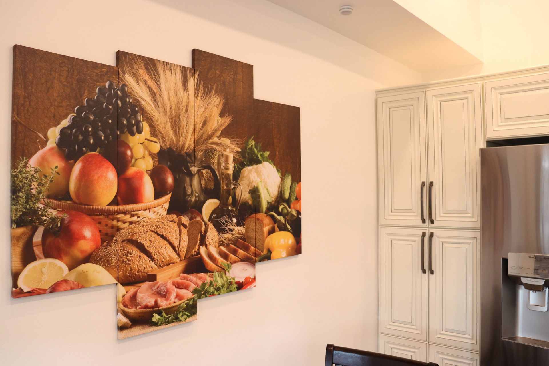 A kitchen with a painting of fruits and vegetables on the wall.