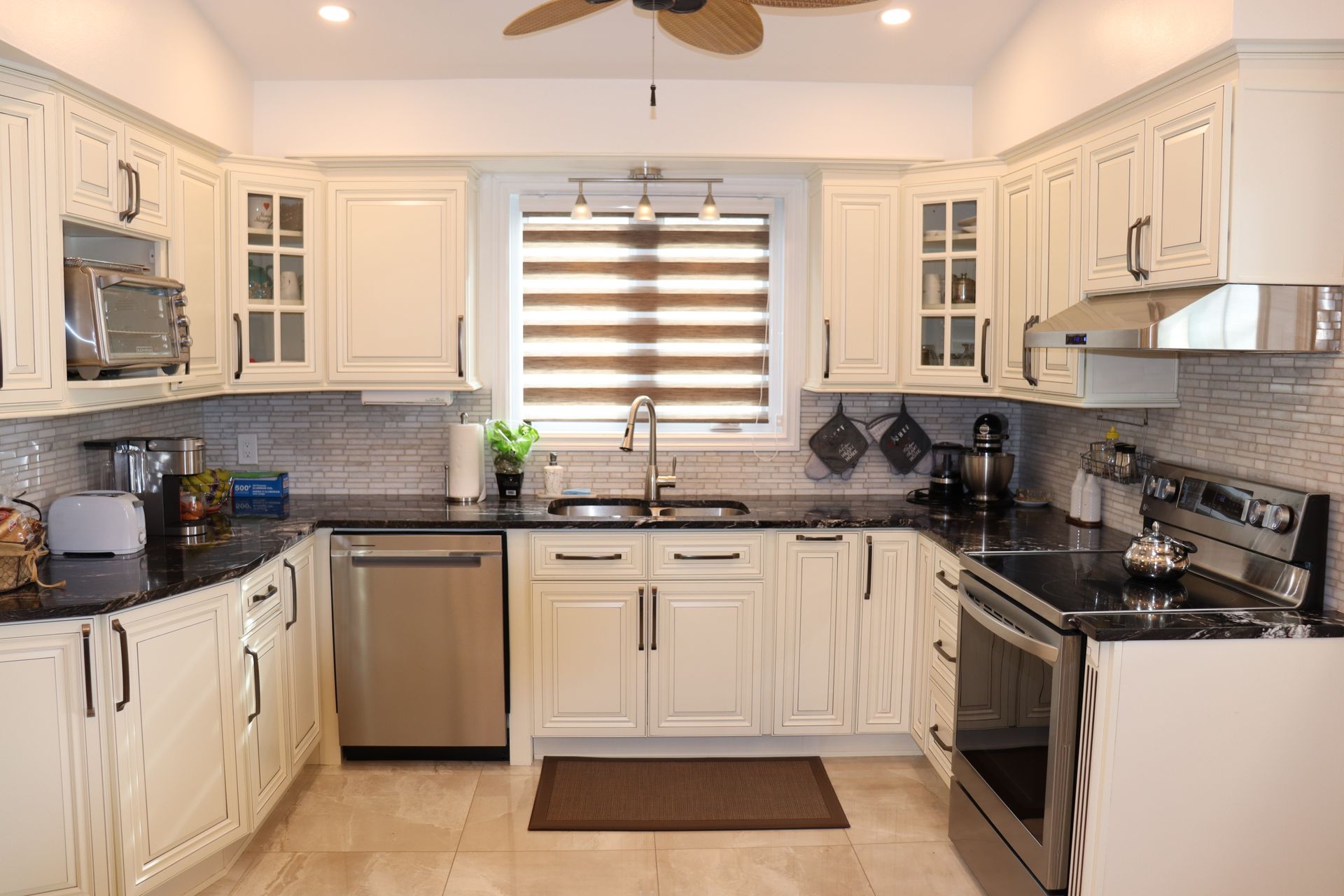A kitchen with white cabinets , black counter tops , stainless steel appliances and a ceiling fan.