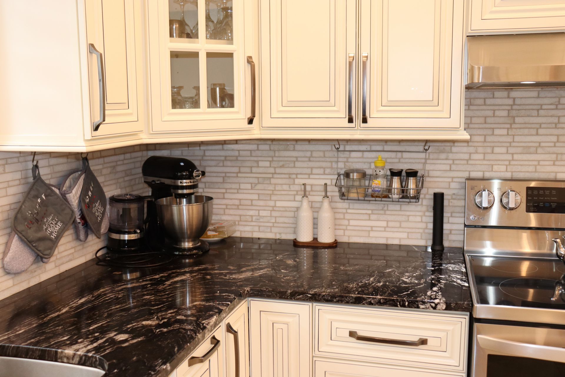 A kitchen with white cabinets , black counter tops , a stove , and a mixer.