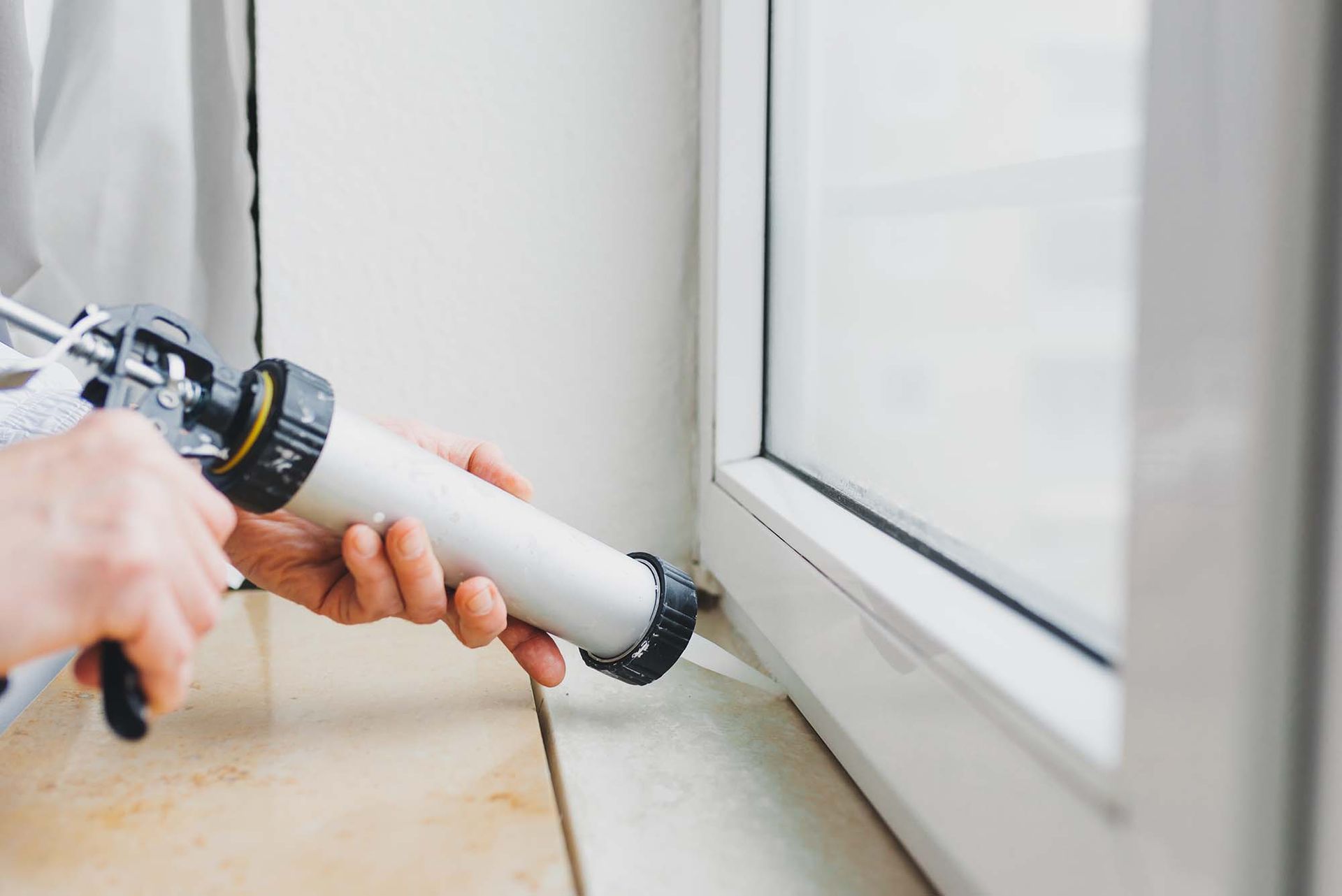 Caulking a white window frame with a caulking gun near the sill