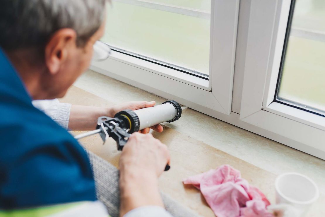 Person applying sealant with a caulking gun along a window sill indoors