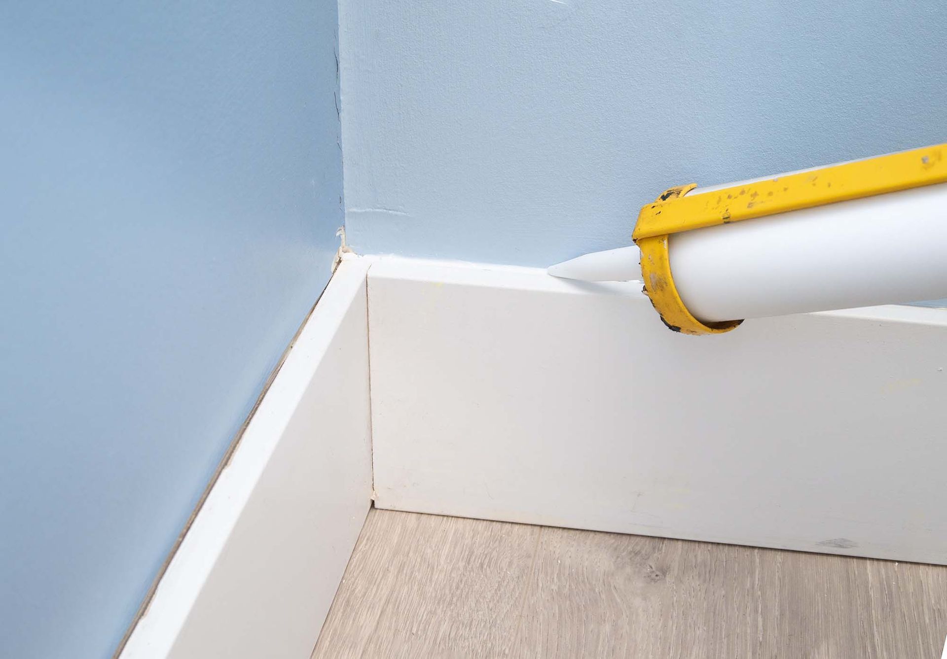 Close-up of a blue wall corner with white baseboard and a yellow-and-white pipe or hose on the right