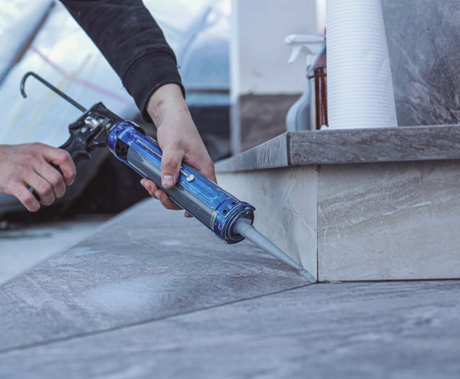 Person applying sealant to a concrete roof seam with a caulking gun