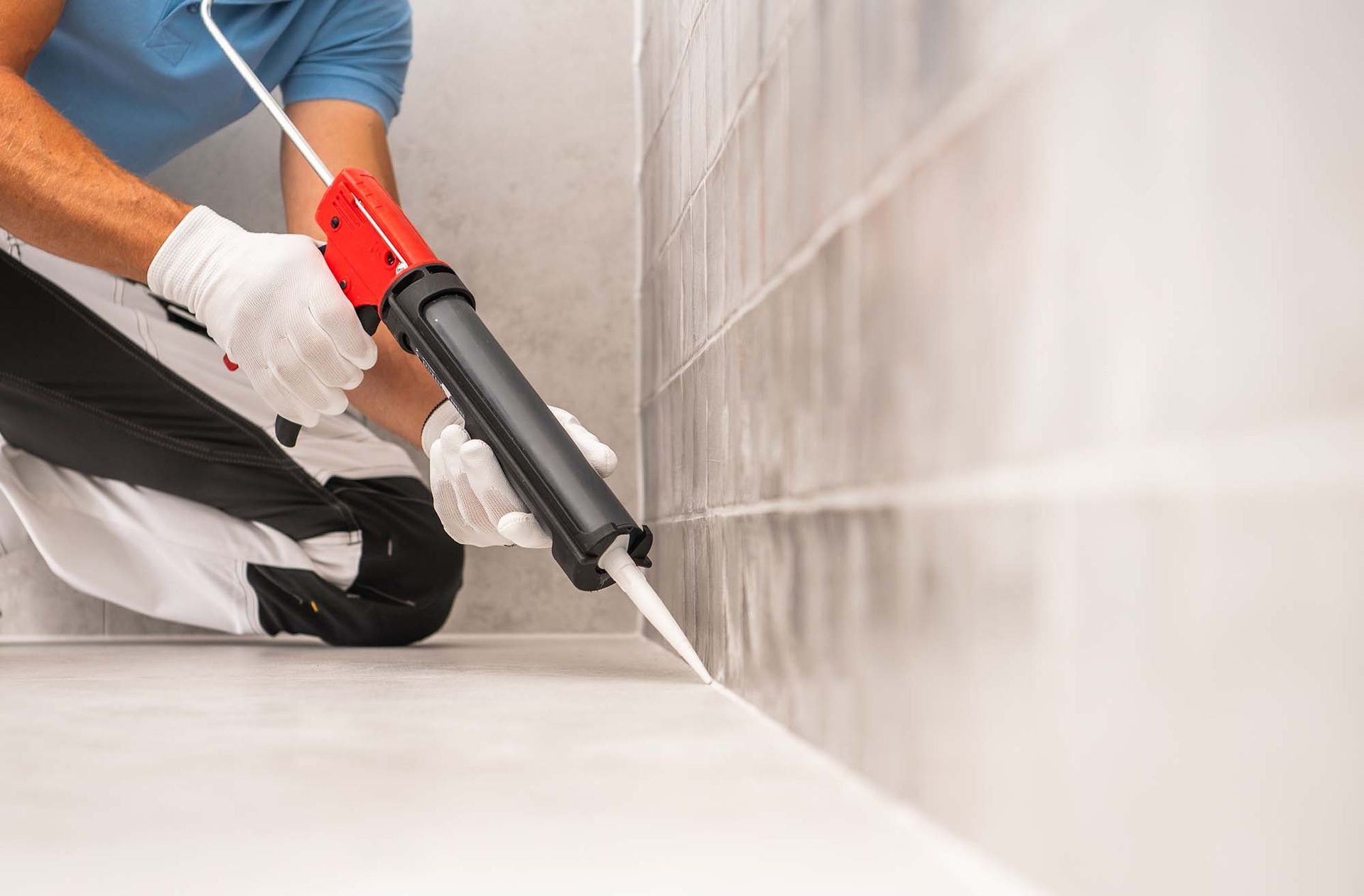 Worker applying sealant to a tiled wall with a red caulking gun