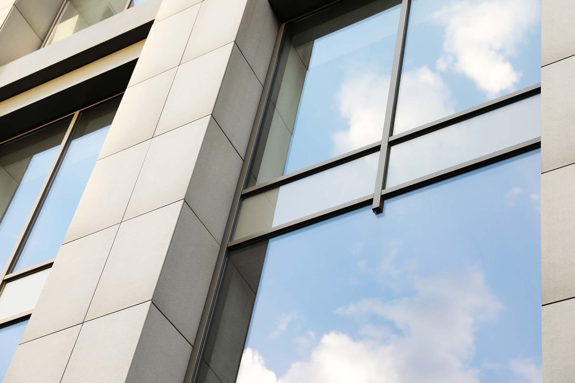 Modern building facade with reflective glass windows and gray stone panels against a blue sky.