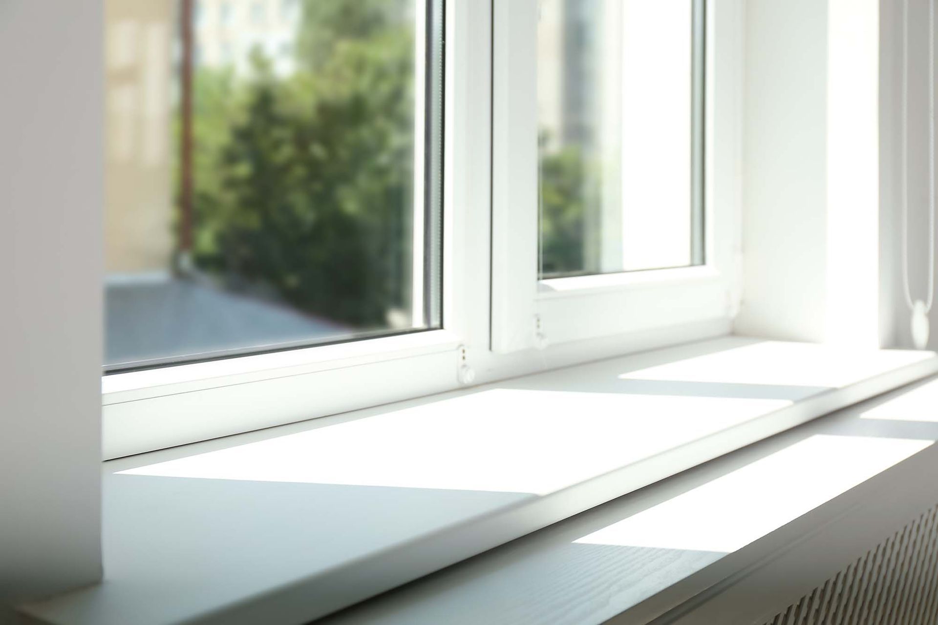 Bright white windowsill by an open window with sunlight and a blurred green view outside