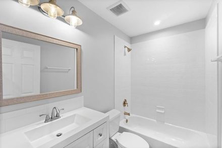 Bright white bathroom with vanity, mirror, tub, and shower combo, lit by three ceiling lights