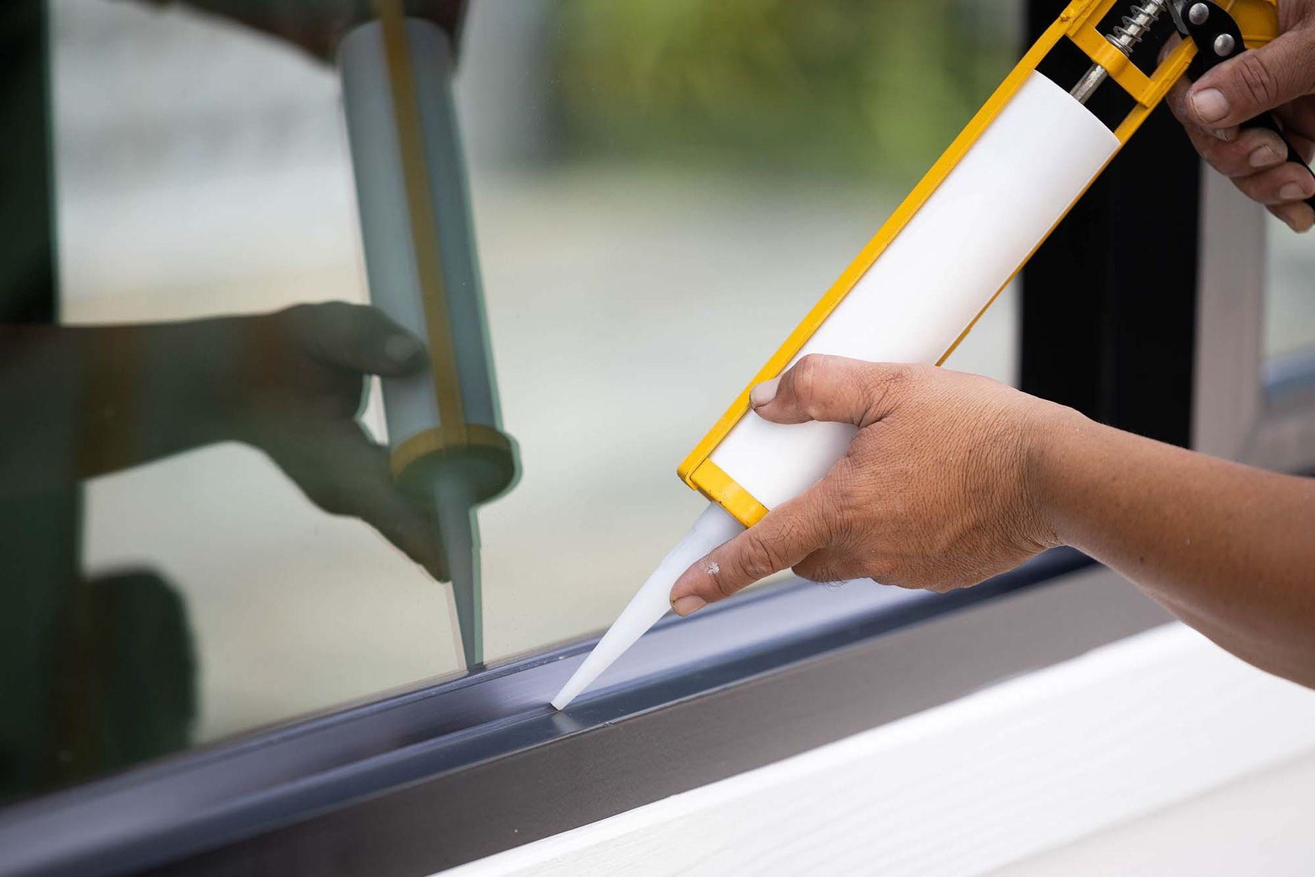 Hand applying caulk with a yellow caulking gun along a window seam