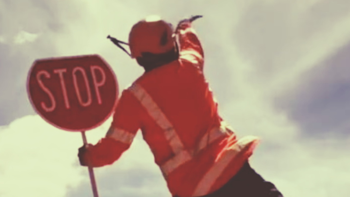 Person in orange safety gear holding a stop sign against a bright sky