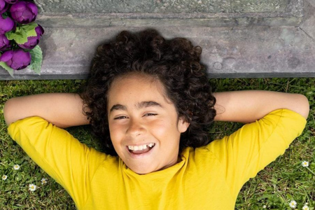 Person lying on grass with hands behind head, smiling in a bright yellow shirt.