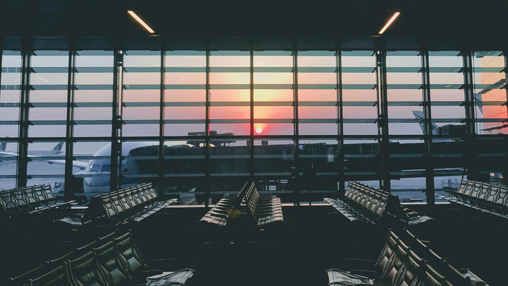 Airport terminal seating facing a sunset through large floor-to-ceiling windows