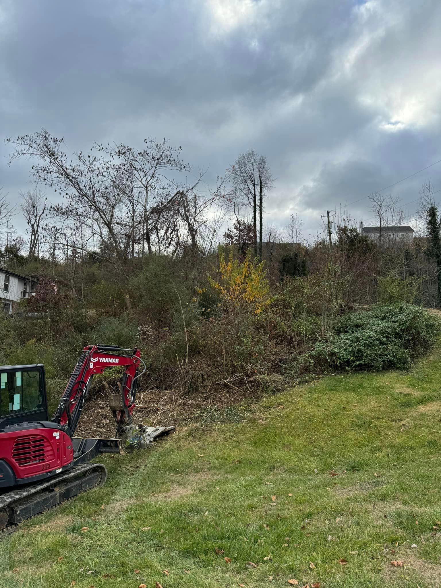 A red excavator is sitting in the middle of a grassy field.