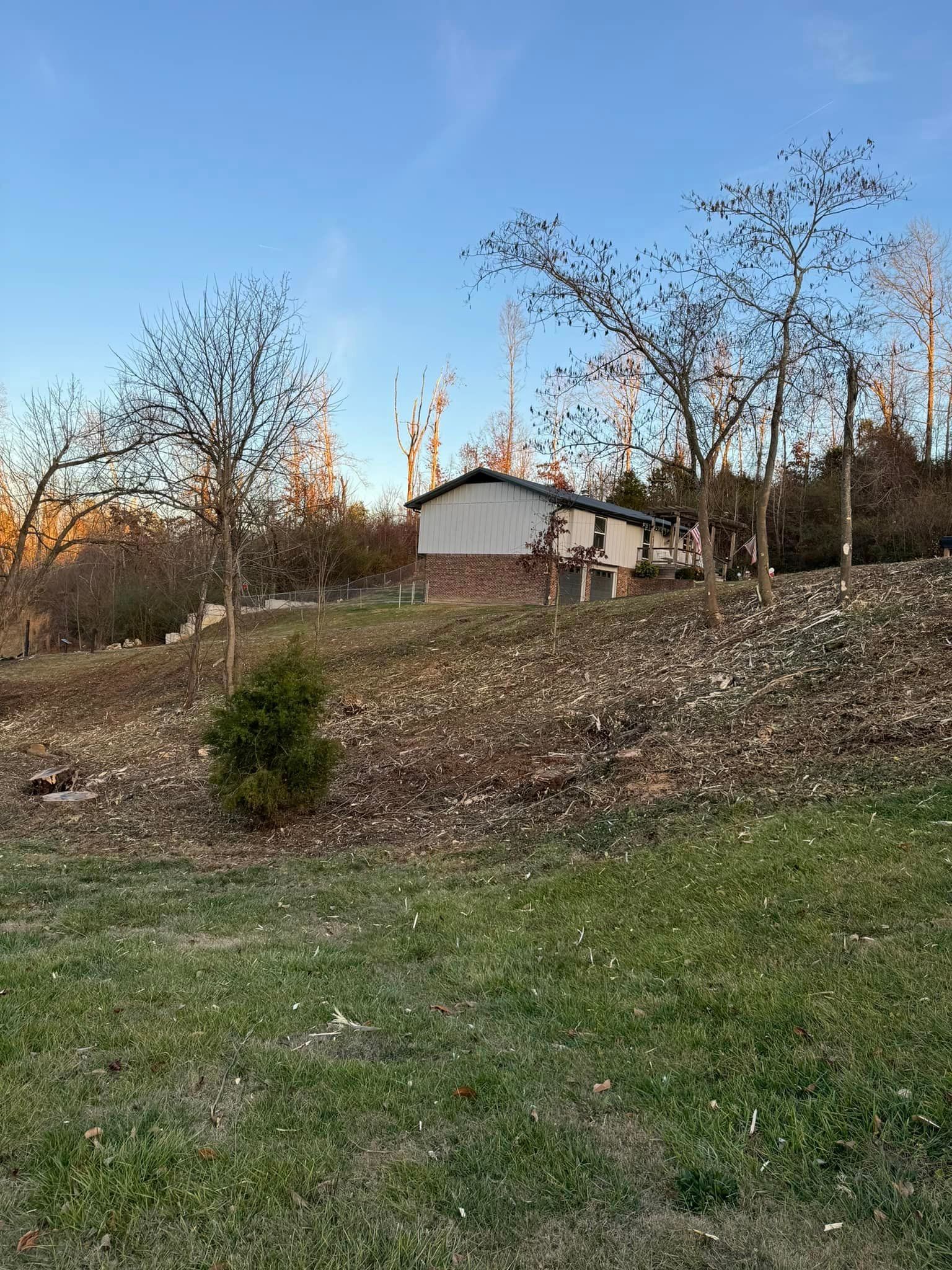 A house is sitting on top of a hill in the middle of a field surrounded by trees.
