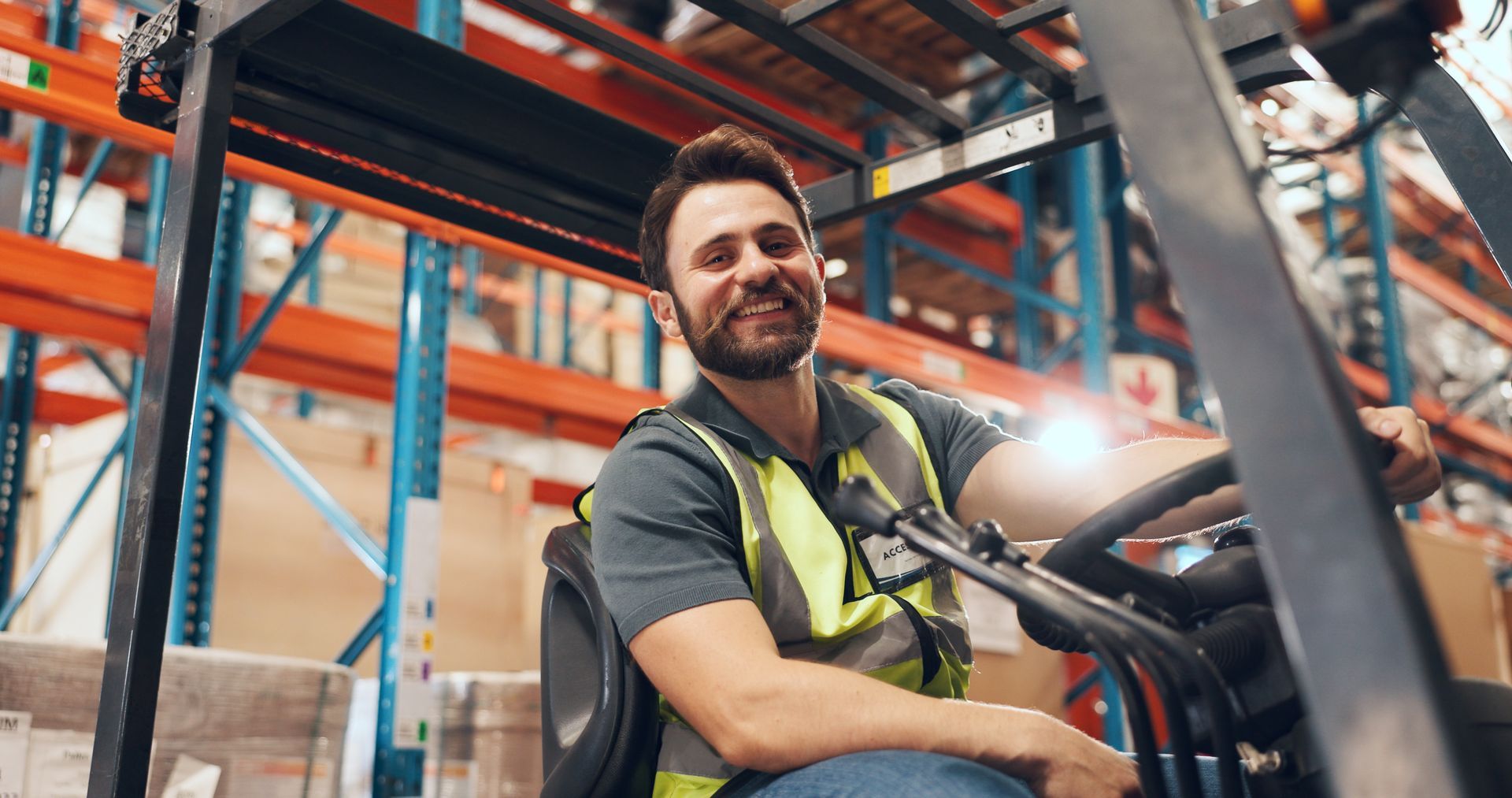 Warehouse worker operating a forklift in a distribution center aisle. Warehouse worker operating a forklift in a distribution center aisle.