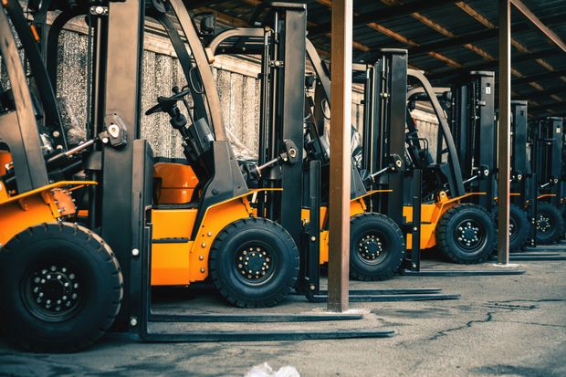 Row of parked yellow and black forklifts under a corrugated metal shelter.