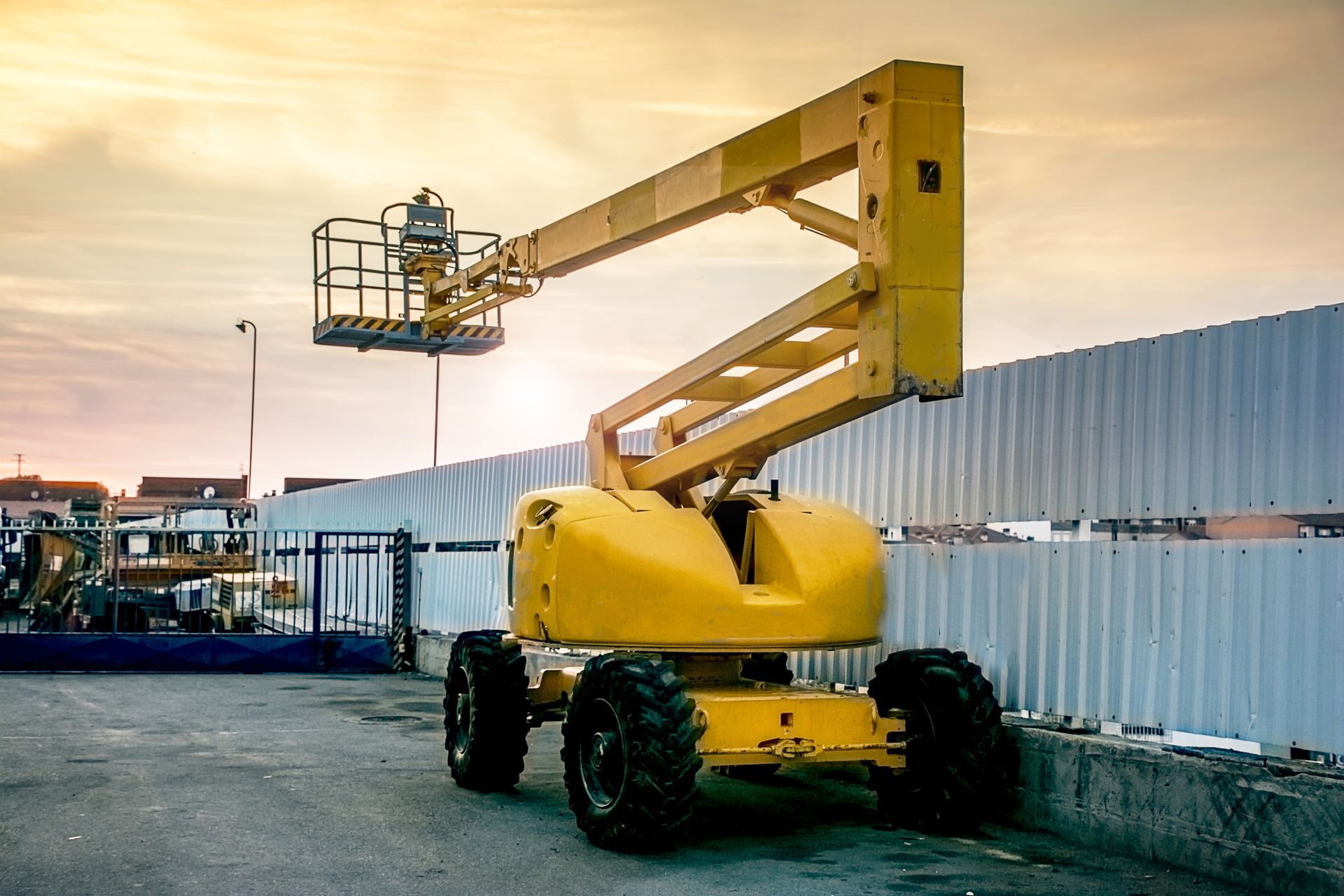Yellow boom lift parked beside a corrugated metal fence at a worksite during sunset Yellow boom lift parked beside a corrugated metal fence at a worksite during sunset