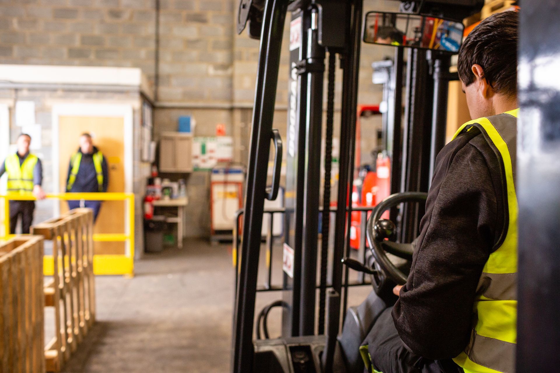 Operator in a hi-vis vest driving a forklift past stacked pallets inside a warehouse