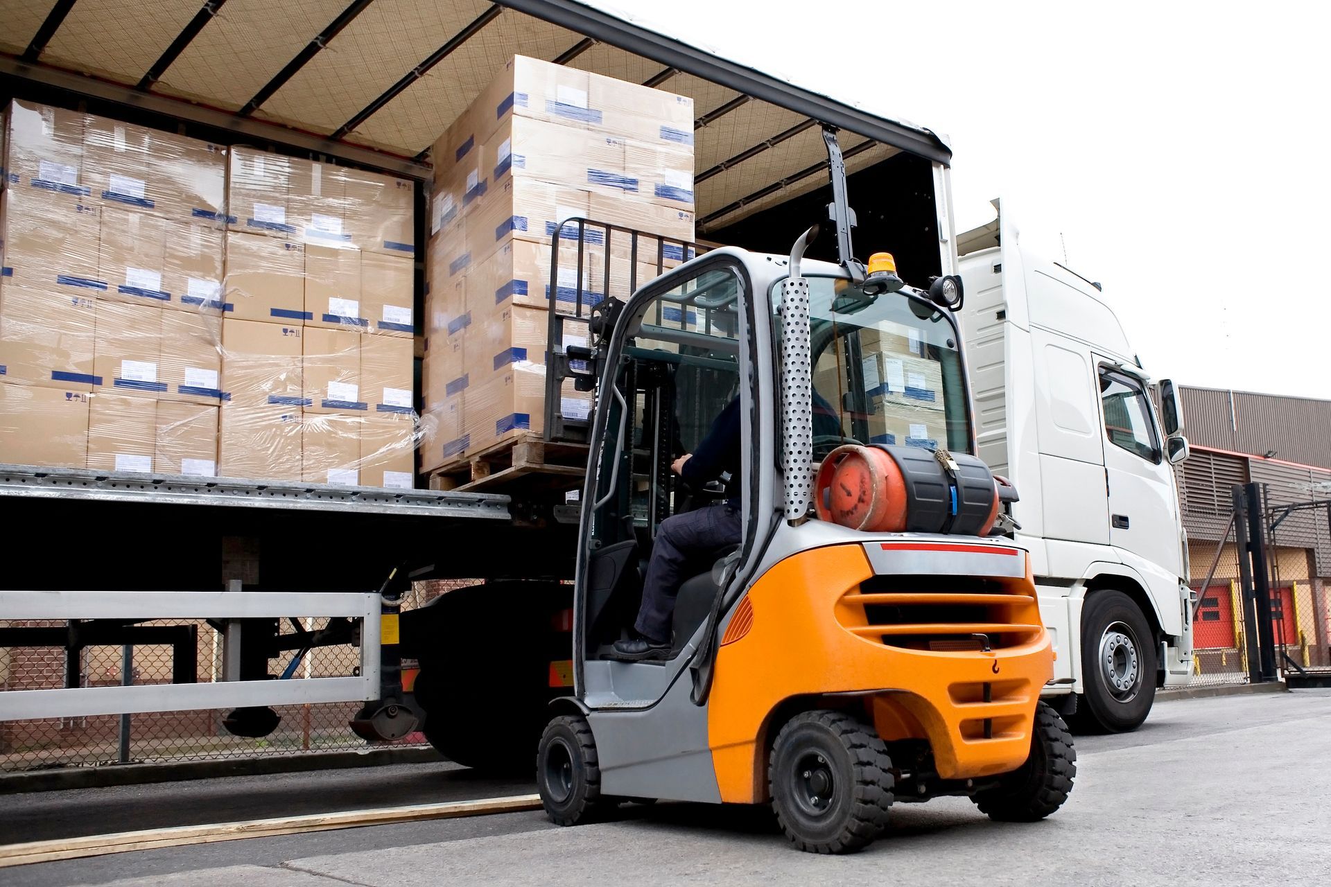 Forklift lifts stacked pallets from a truck trailer during a warehouse loading operation. Forklift lifts stacked pallets from a truck trailer during a warehouse loading operation.
