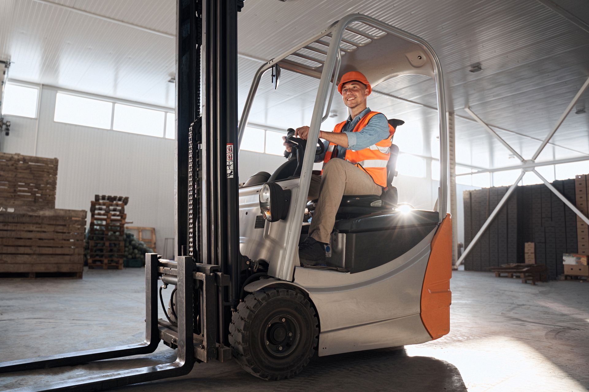 Man operating a forklift, carrying a pallet with a large cardboard box inside a warehouse. Man operating a forklift, carrying a pallet with a large cardboard box inside a warehouse.