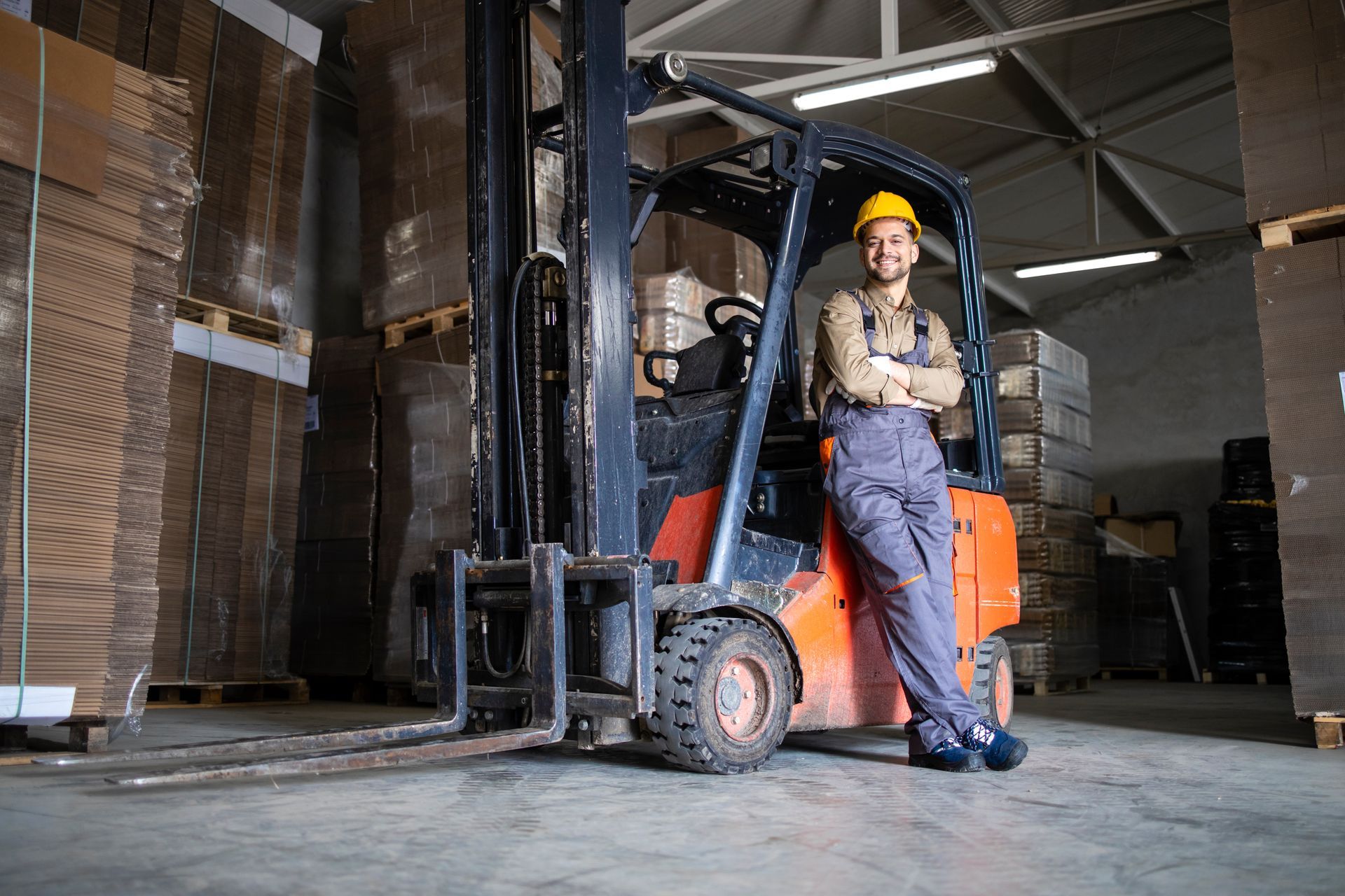 Warehouse worker standing beside a forklift among stacked pallets and boxes. Warehouse worker standing beside a forklift among stacked pallets and boxes.