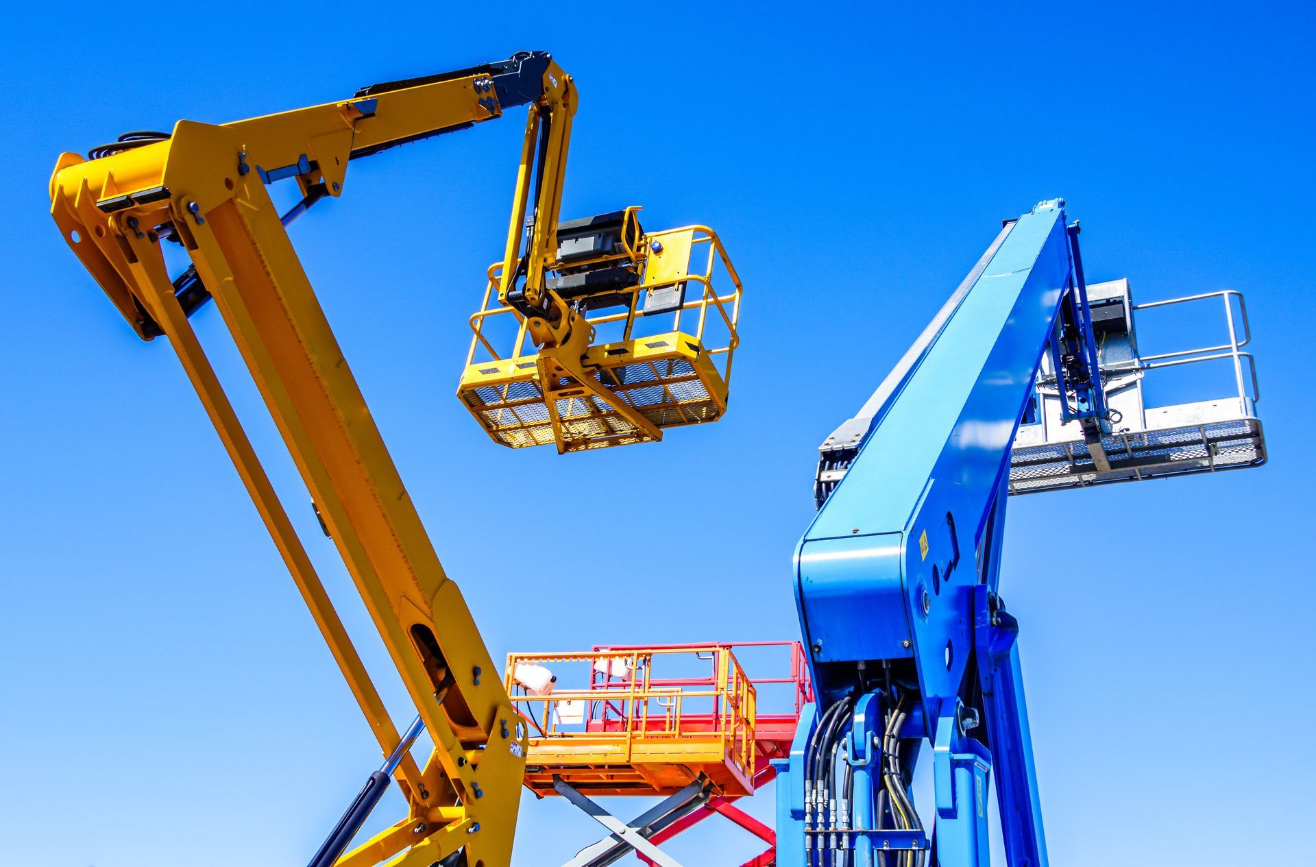 Telescoping and articulating boom lifts against a clear blue sky Telescoping and articulating boom lifts against a clear blue sky