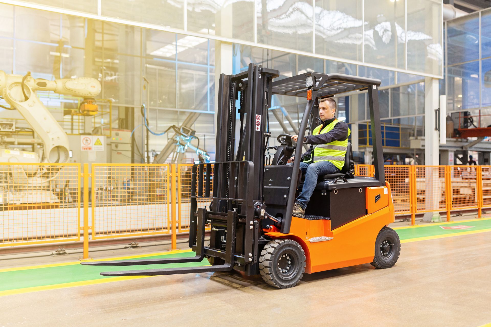 Forklift operator in a factory, wearing a safety vest. Orange forklift on a factory floor with machinery. Forklift operator in a factory, wearing a safety vest. Orange forklift on a factory floor with machinery.