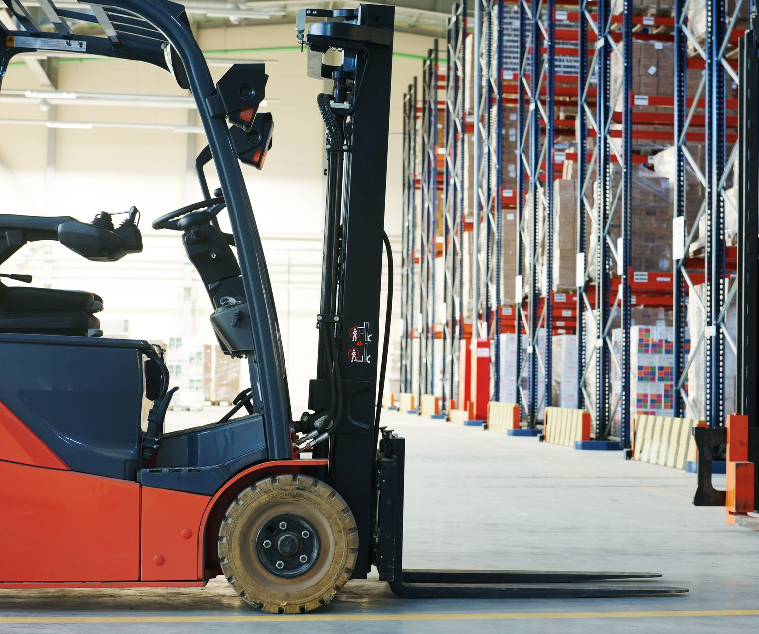 Forklift in warehouse aisle, orange and gray, with shelves of stacked boxes in the background. Forklift in warehouse aisle, orange and gray, with shelves of stacked boxes in the background.