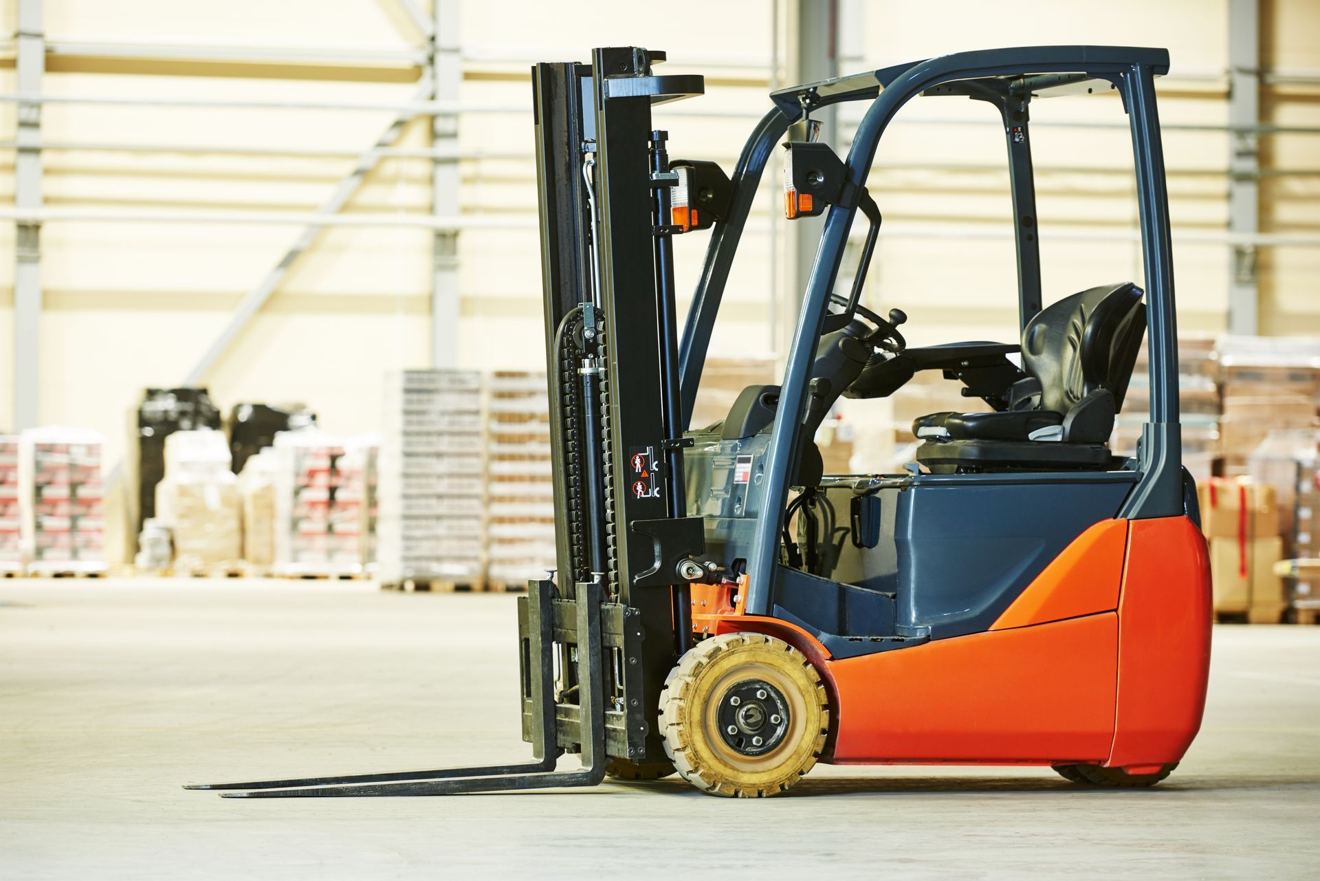 Forklift in warehouse; blue and orange, ready for use, pallets in background. Forklift in warehouse; blue and orange, ready for use, pallets in background.