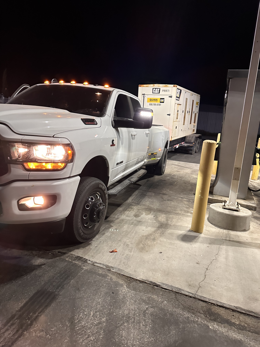 White pickup truck towing a generator trailer at night; headlights and amber lights are on.