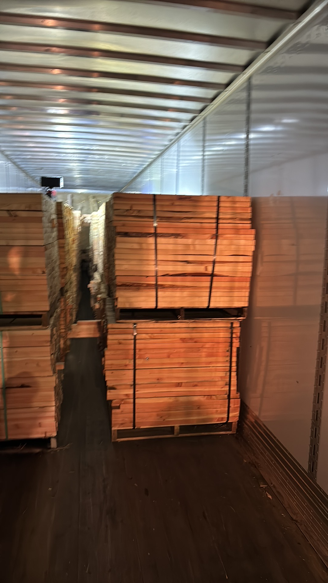 Stacks of wooden planks secured on pallets inside a cargo trailer.