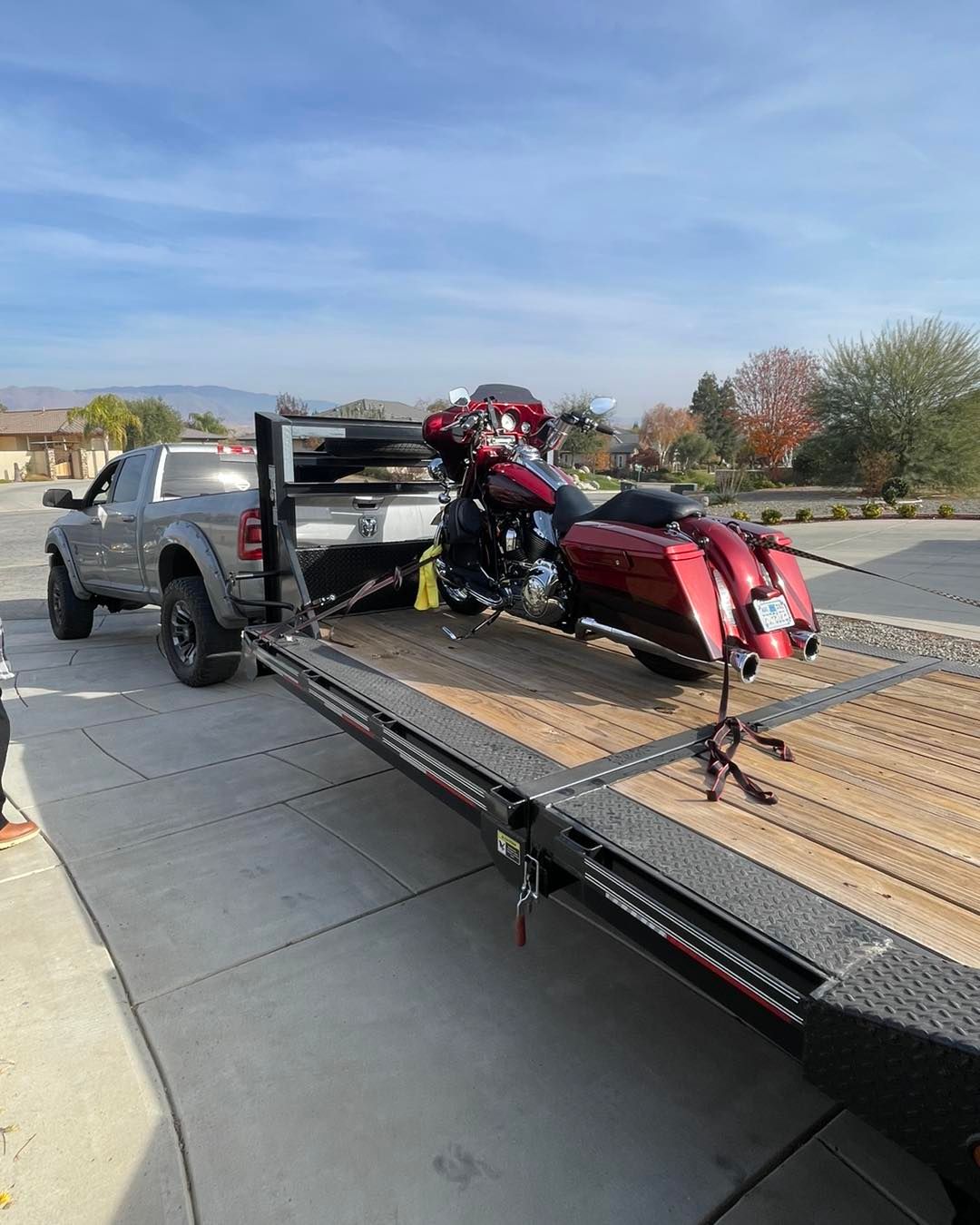 A red motorcycle secured on a flatbed trailer hitched to a gray pickup truck in a residential area.