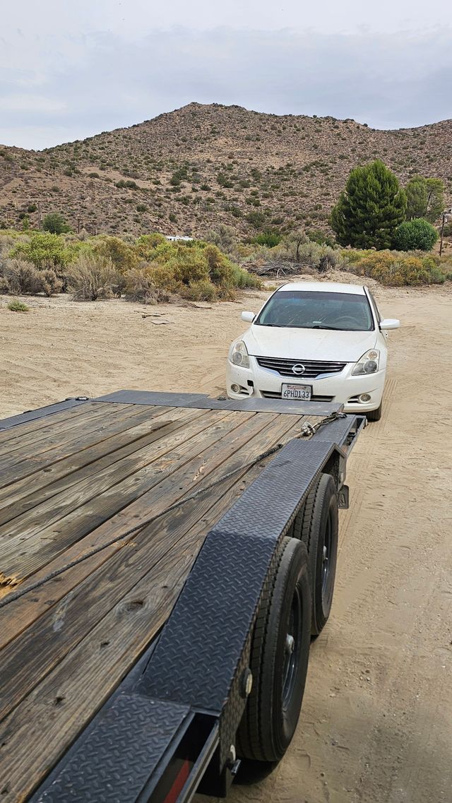 White car on a trailer in a desert landscape with a rocky mountain in the background.