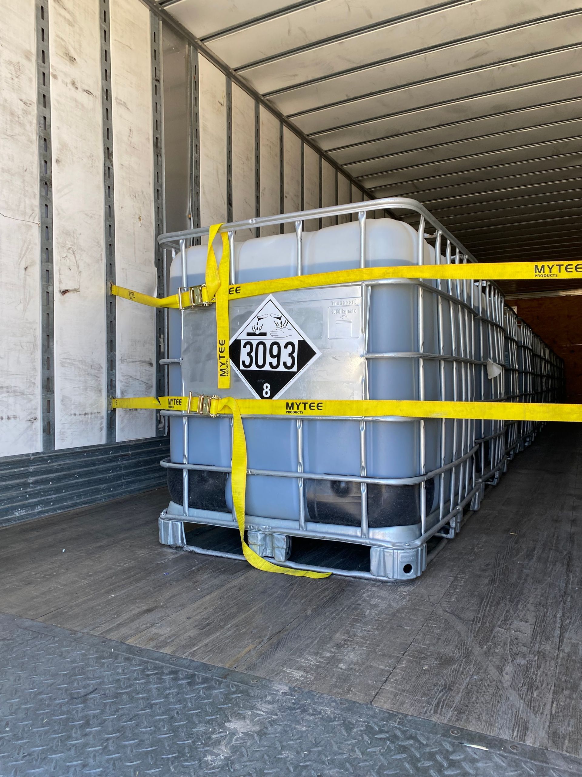 A large tank with hazardous materials label 3093 secured inside a truck with yellow straps.
