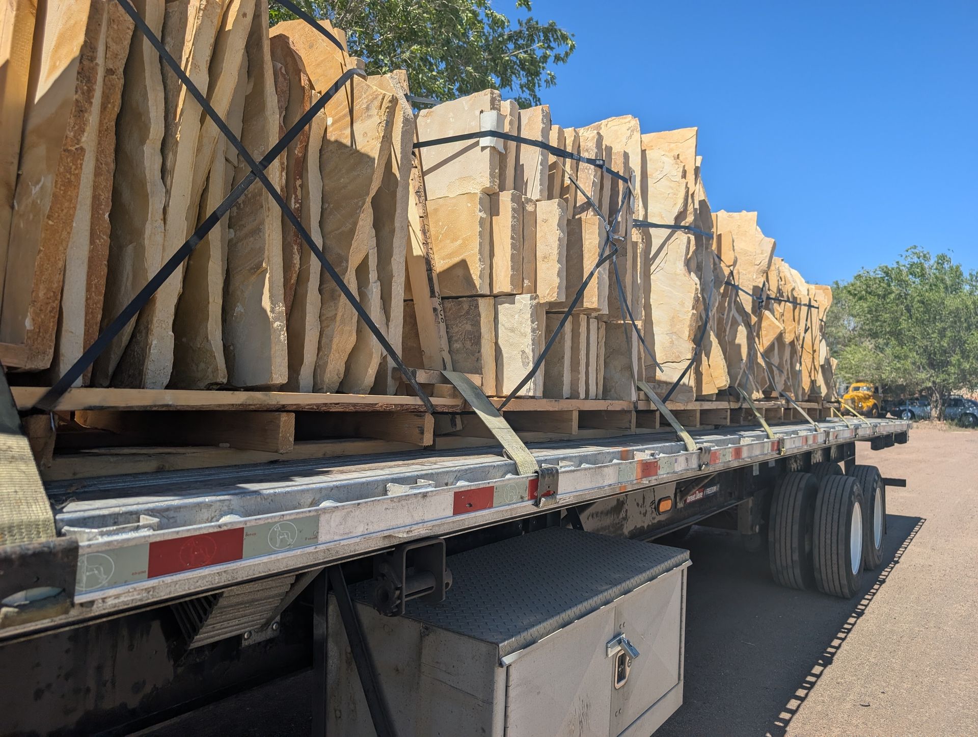 Flatbed truck carrying stacked pallets of beige stone slabs, secured with straps.