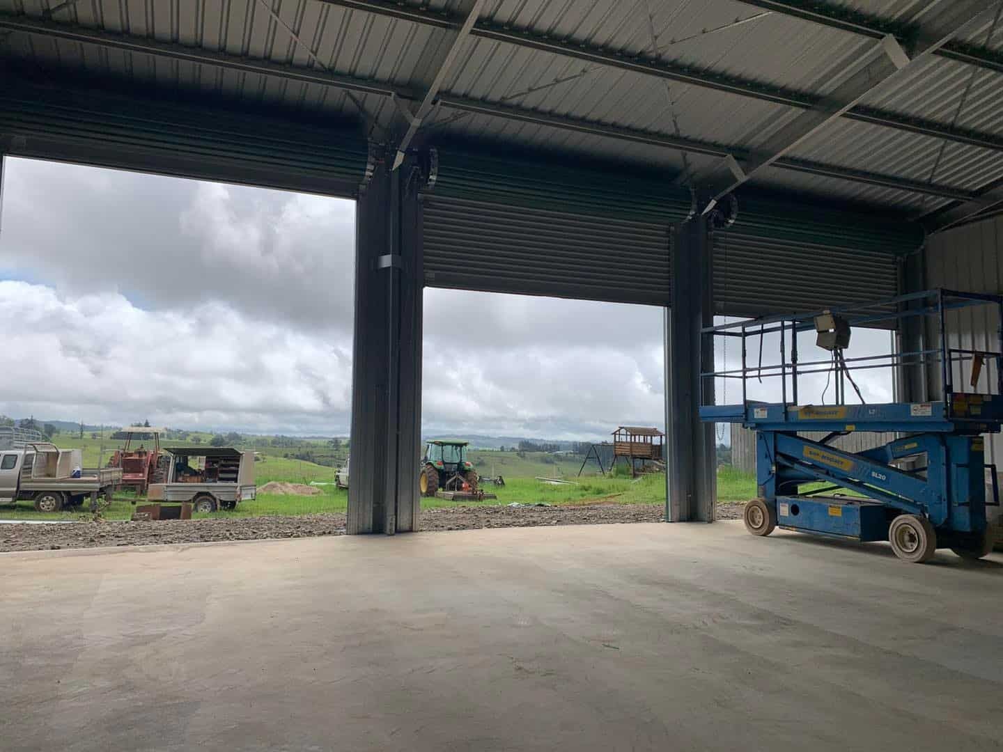 Inside a Metal Warehouse, Two Open Roll-up Doors Reveal a Grassy Field — ShedBoss in Atherton, QLD