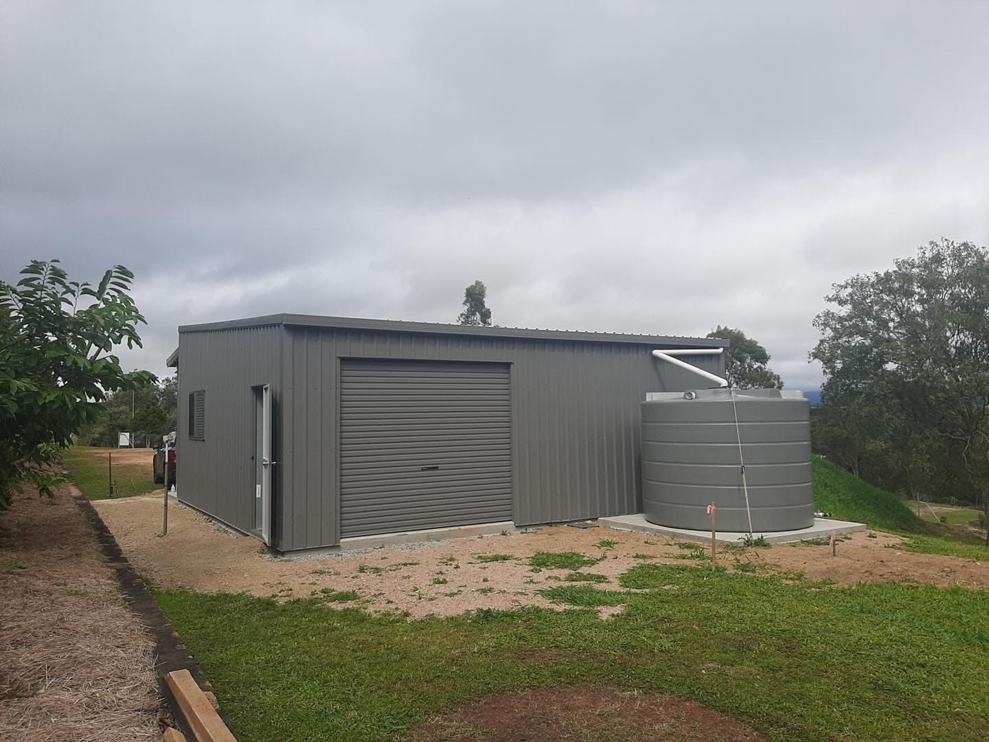 Gray Metal Shed With a Roller Door and Water Tank — ShedBoss in Atherton, QLD