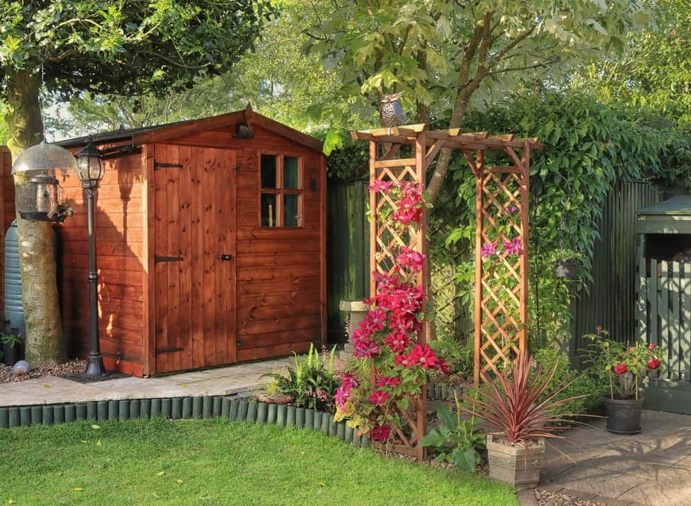 Wooden Garden Shed, Trellis With Red Flowers, Green Lawn and Foliage, Stone Path — ShedBoss in Atherton, QLD