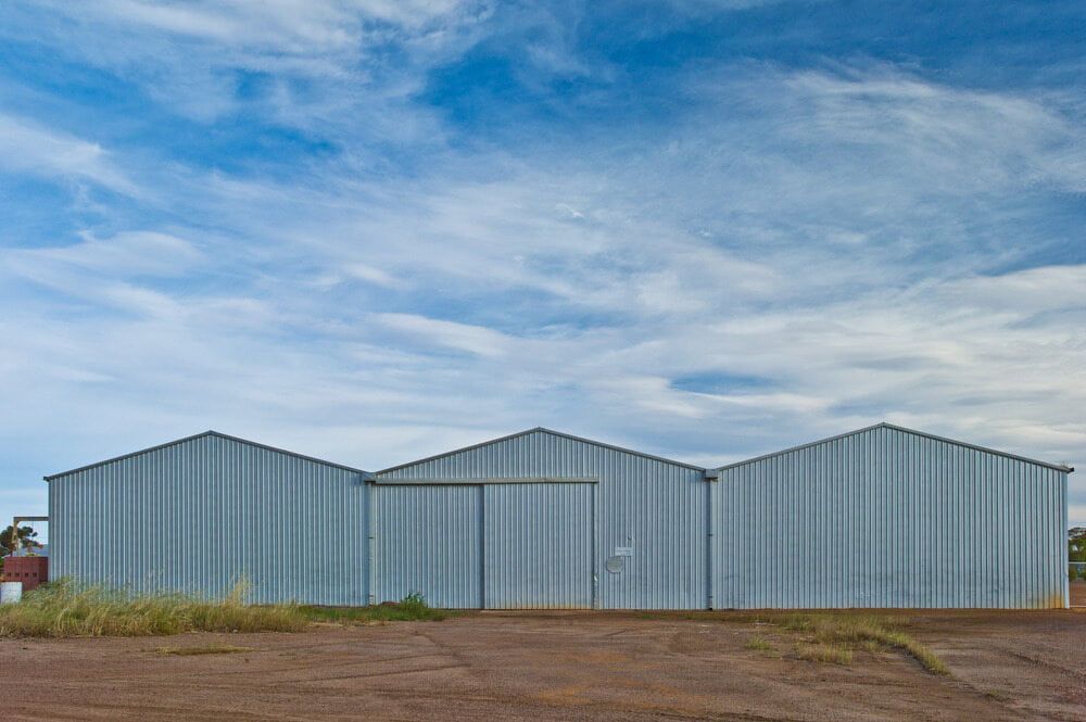Three Silver Metal Warehouses With Pointed Roofs Against a Cloudy Blue Sky — ShedBoss in Yungaburra, QLD 