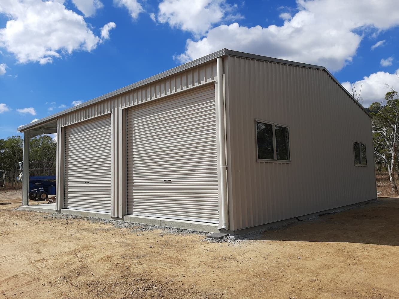 Tan Metal Shed With Two Roller Doors, Windows, and a Blue Sky Background — ShedBoss in Atherton, QLD