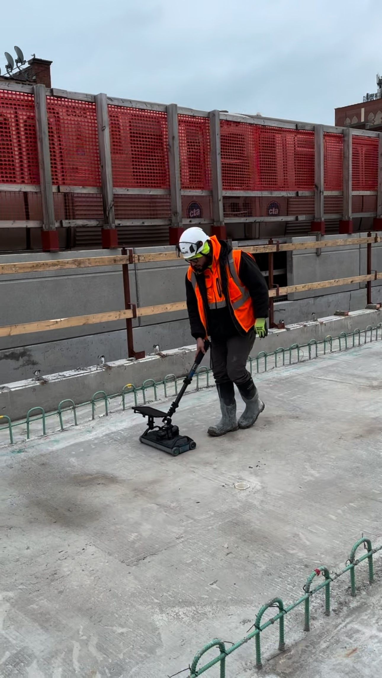 Construction worker in orange vest uses a device on concrete surface.