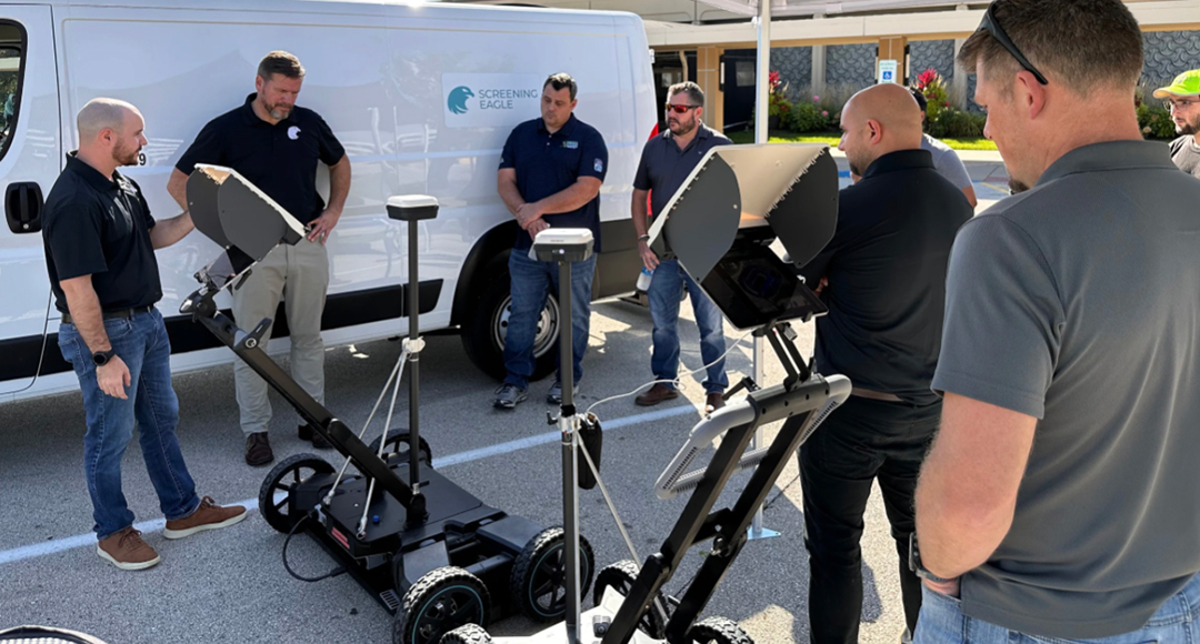 Group of men with surveying equipment near a white van, outdoors.